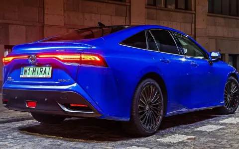 Niebieska Toyota Mirai z podświetlonymi światłami tylnymi stoi na brukowanej ulicy nocą.