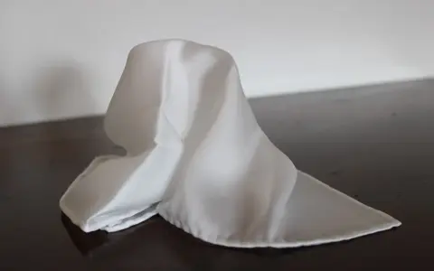Un fazzoletto bianco di seta, drappeggiato su un tavolo scuro. Il suo significato è legato alla purezza e all'eleganza.