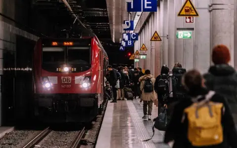 Pasażerowie czekają na czerwony pociąg DB na peronie. Zastanawiasz się, ile zarabia konduktor PKP?