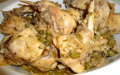 Piatto fumante di coniglio alla cacciatora in bianco, con olive verdi e erbe aromatiche. Un classico della cucina italiana.