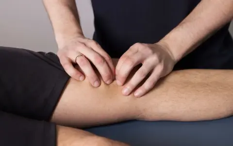 Fizjoterapeuta wykonuje masaż kolana, co jest częścią leczenia chondropatii rzepki.