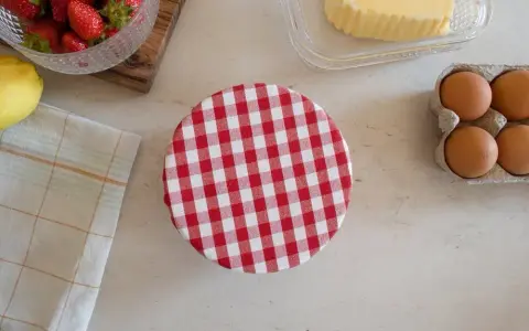 Préparation d'une charlotte alimentaire : fraises, citron, beurre, œufs et un couvercle à carreaux rouges et blancs.