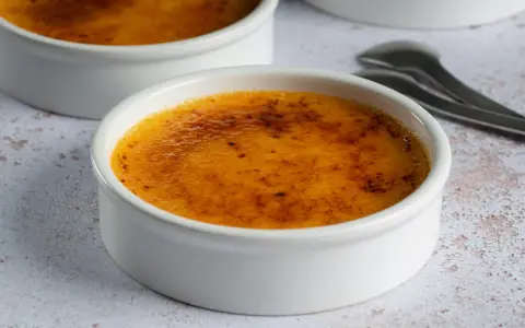 Dwa kremowe desery w białych naczyniach, z chrupiącą, karmelizowaną skórką. Crème brûlée czy crema catalana? Wybór należy do Ciebie!