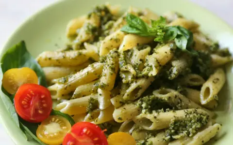 Penne z pesto i pomidorkami koktajlowymi. Pyszny obiad bez mięsa, udekorowany listkami bazylii.