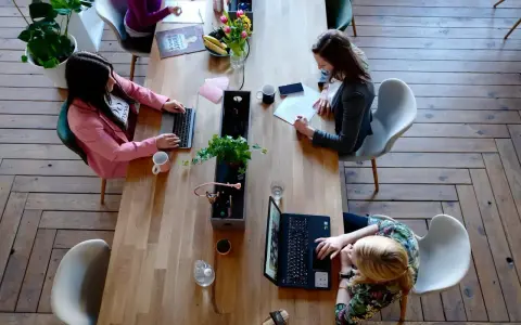 Kobiety pracują przy drewnianym stole. Jedna pisze na laptopie, druga notuje. To przykład, jak etyka co to, wpływa na codzienne zadania.