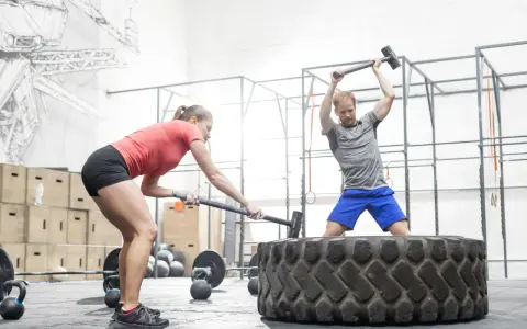 Kobieta i mężczyzna ćwiczą z młotami na oponie w siłowni CrossFit.