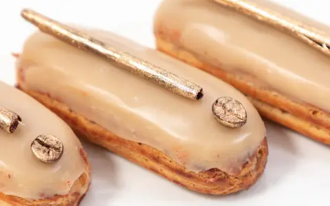 Trois éclairs gourmands, glacés à la crème pâtissière café, ornés d'une touche dorée et d'un grain de café scintillant.