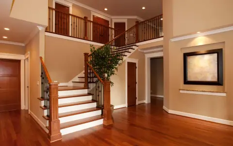 Interno di una casa due piani moderna: scala in legno e metallo, porte in legno, un quadro e un albero decorativo.