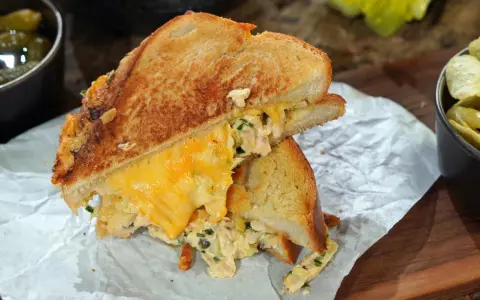 Ein köstlicher Tuna Melt mit geschmolzenem Käse, serviert mit Gurken und Chips.