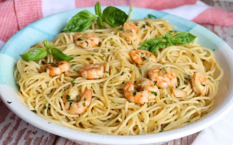 Un plato de espaguetis con gambas, adornado con hojas de albahaca fresca y perejil picado.