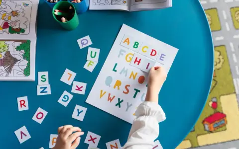 Dziecko układa kolorowy alfabet pisany na niebieskim stole. Obok leżą luźne literki i książeczka do kolorowania.