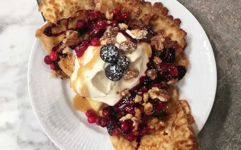Frasiga pannkakor toppade med vispgrädde, bär, nötter och sirap. En härlig frukost eller dessert.