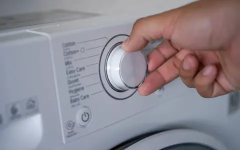Mano ajustando el selector de la lavadora para saber como lavar un anorak. Se ven programas como "Cotton", "Mix", "Duvet".