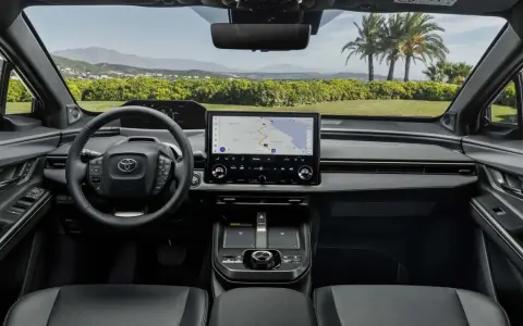 Interni moderni della Toyota bz4x con ampio display centrale e volante multifunzione. Navigazione attiva per un viaggio panoramico.