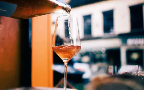 En flaska häller upp ett bubbligt, roséfärgat pet nat i ett elegant glas. En härlig kväll väntar.