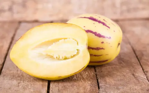 Eine Melonenbirne, die nicht giftig ist, wird auf Holzbrettern präsentiert. Eine Hälfte zeigt das saftige Fruchtfleisch.