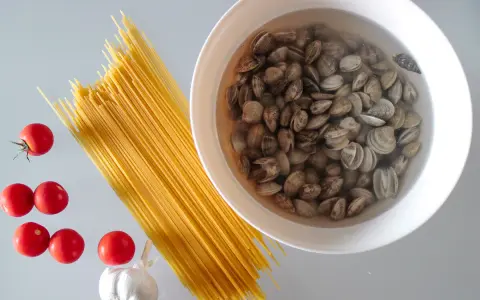 Składniki na pyszny makaron z małżami: spaghetti, pomidorki, czosnek i świeże małże w misce.