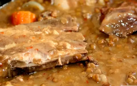Guiso de lentejas con costillas, zanahoria y trozos de carne en un caldo espeso.