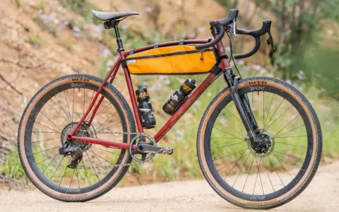 A red gravel bike with an orange frame bag and two water bottles. This bike, like many gravel bikes, does not have suspension, relying on its tires and frame for comfort.