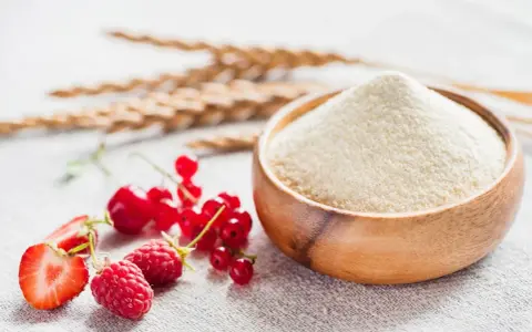 Miseczka z semoliną, obok świeże owoce: truskawki, maliny, porzeczki. Zboża w tle. Semolina co to? To mąka z pszenicy durum.