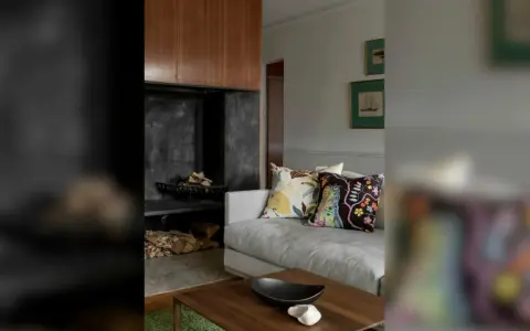 En soffa med färggranna kuddar framför en öppen spis med ved. En stilfull inredning som påminner om Josephine Blix design.