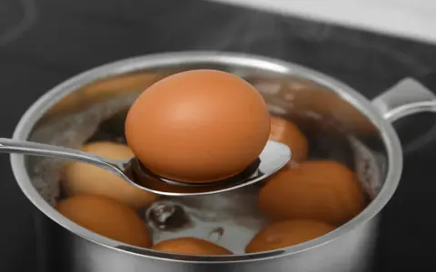 Łyżka z jajkiem nad garnkiem z gotującą się wodą. W ten sposób można łatwo dowiedzieć się, jak sparzyć jajka.