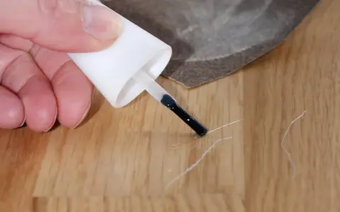 Mit einem Lackstift und Schleifpapier werden Kratzer auf dem Laminat repariert.