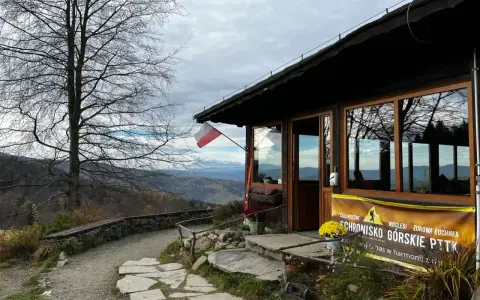 Bacówka pod Wierchomlą, schronisko górskie PTTK z widokiem na góry. Polska flaga powiewa nad wejściem.