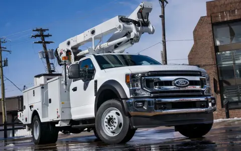 Biały Ford F-750 z podnośnikiem koszowym gotowy do pracy przy liniach energetycznych.