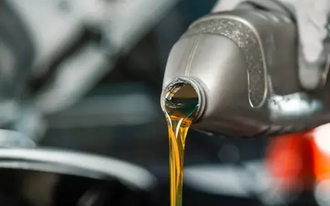 Huile moteur dorée versée d'une bouteille, illustrant la viscosité.