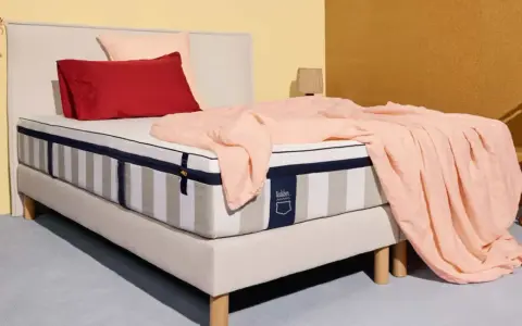 Un matelas rayé, drapé d'une couverture rose pâle, avec des coussins rouge et rose. La question est : combien de ressorts pour un bon matelas ?