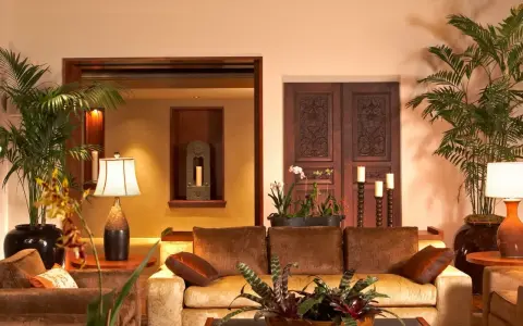 Salotto accogliente con divani in velluto, piante tropicali e porte intagliate in legno scuro, che evocano un caldo **stile coloniale**.