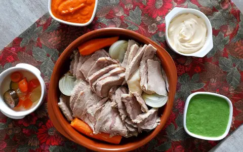 Un invitante bollito di carne, affettato e servito con carote, cipolle e tre salse: una rossa, una bianca e una verde.