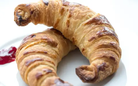 Två gyllene croissants med vaniljfyllning ligger på en vit tallrik. En klick hallonsylt bredvid.