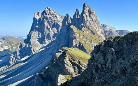 Majestätische Felszinnen ragen in den blauen Himmel. Eine **Seceda Wanderung** führt durch grüne Almwiesen und felsiges Gelände.