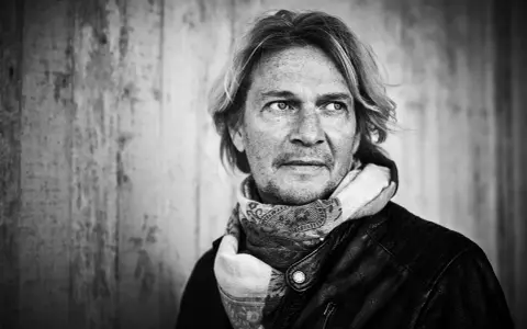 Tommy Nilsson, med sitt karaktäristiska utseende och en scarf, redo att inta scenen med sitt band.