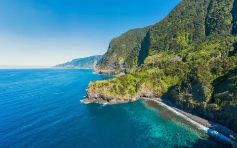 Grüne Berghänge stürzen ins türkisfarbene Meer. Ein perfekter Tag für eine Reise nach Madeira im Oktober.