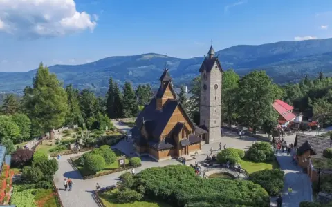 Drewniany kościółek i wieża na tle gór. Czy to Karpacz, czy Szklarska Poręba?