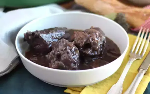 Un plat de coq au vin mijoté, servi dans un bol blanc, avec une fourchette et un couteau à côté.