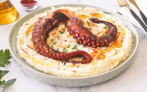 Delicioso pulpo a la brasa sobre puré de patatas cremoso, espolvoreado con pimentón y perejil.