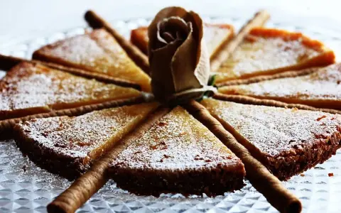 En vacker vit kladdkaka uppskuren i tårtbitar, dekorerad med en pappersros och chokladrullar.
