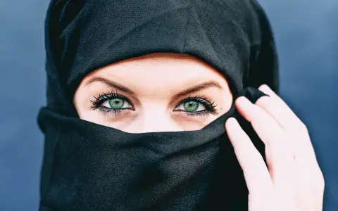 Ein schwarzes Kopftuch umrahmt ein Gesicht, dessen grüne Augen durch den Stoff blicken. Die Bedeutung von Kopftuchfarben ist vielfältig.