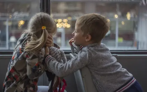 Bambina con disturbo della comunicazione sociale si nasconde, mentre un bambino le parla con un sorriso.