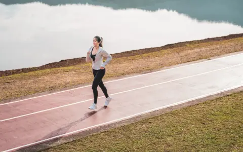 Une femme souriante profite d'une marche rapide sur une piste de course, au bord d'un lac paisible.