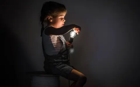 Niña con miedo a la oscuridad, sentada en un rollo de cable, sosteniendo una bombilla encendida.