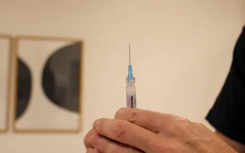 En hand håller en spruta med en droppe vaccin redo för injektion. Kanske en del av vaccin Singapore-programmet.