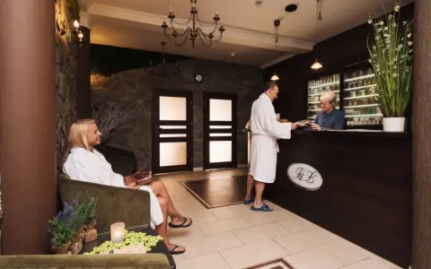 Recepcja w hotelu dla dorosłych. Kobieta w szlafroku siedzi, mężczyzna rozmawia z pracownikiem.