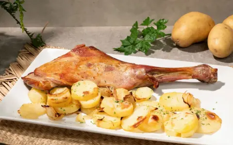 Paletilla de cordero al horno dorada y jugosa, acompañada de patatas panadera y perejil fresco. Un plato principal delicioso.