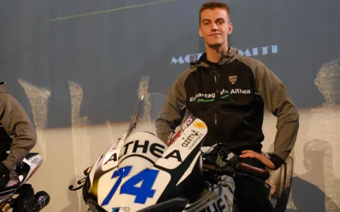 Piotr Biesiekirski, młody kierowca wyścigowy, pozuje obok swojego motocykla z numerem 14.