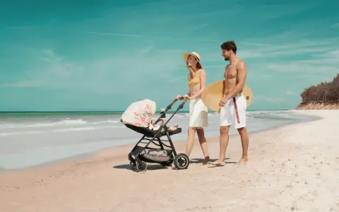 Para spaceruje po plaży z wózkiem Kinderkraft Askoy. Mężczyzna niesie deskę surfingową.